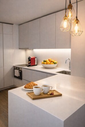 A modern kitchen with a central island, a bowl of fruit, and a croissant on the counter. - Praça do Comercio Romantic Apartment (Lisboa)
