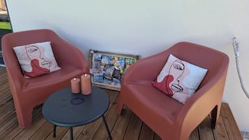 Kaksi punaista tuolia, joissa on samanväriset tyynyt, pieni pyöreä pöytä ja kehystetty kuva puisella terassilla.