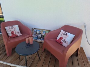 Two red chairs with matching cushions, a small round table, and a framed picture on a wooden deck.