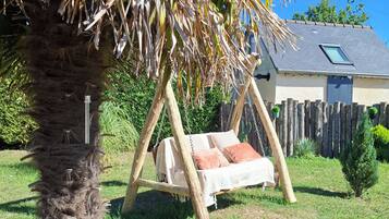 A garden with a swing chair, a palm tree, and a house in the background.