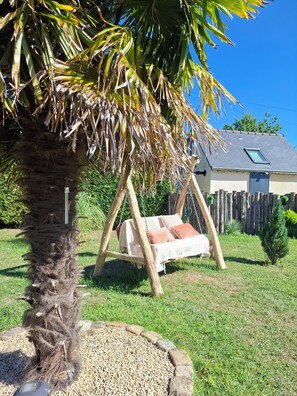Een tuin met een hangstoel, een palmboom en een huis op de achtergrond.