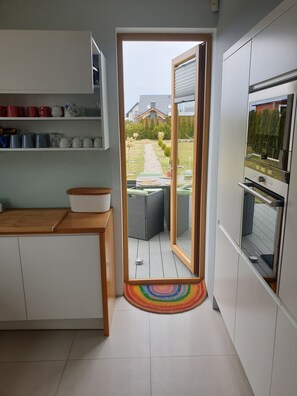 A modern kitchen with a built-in oven, a dining area with a table and chairs, and a view of a garden through an open door. - Villa Near Baltic Sea (2.5 km) – 4 Bedrooms, 3 Bathrooms, Private Garden (Łebcz)