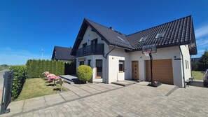 A two-story house with a garage, a basketball hoop, and a well-maintained lawn. - Villa Near Baltic Sea (2.5 km) – 4 Bedrooms, 3 Bathrooms, Private Garden (Łebcz)