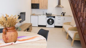 Eine kompakte Küche mit Mikrowelle, Spüle und Waschmaschine. Es gibt einen Essbereich mit Tisch und Stühlen sowie ein Sofa.