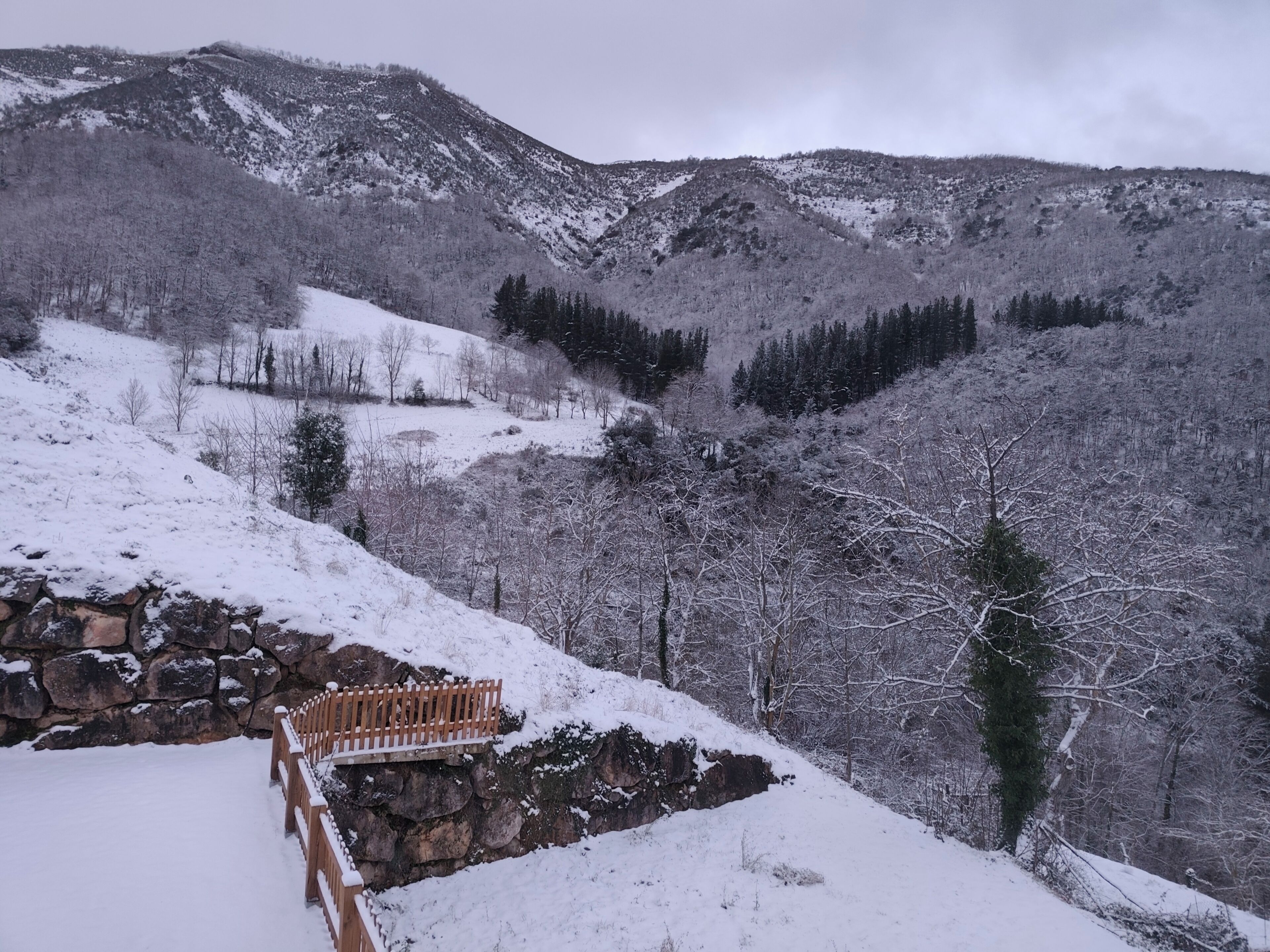 A snowy mountain landscape with a stone wall and wooden fence.