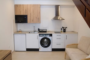 A compact kitchen with a washing machine, microwave, and a built-in stove hood.