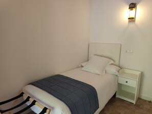 Un lit simple avec une tĂȘte de lit, une table de chevet avec un tiroir et un luminaire fixĂ© au mur.