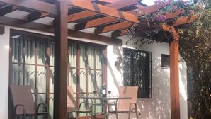 Um alpendre coberto com mesa e cadeiras, um gato e uma pérgula florida.