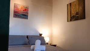Quarto de hotel com uma cama, uma mesa de cabeceira, uma luminária e duas pinturas nas paredes.