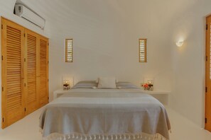 A bedroom with a bed, wooden wardrobe, wall-mounted lights, and an air conditioning unit.