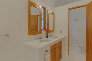 A bathroom with two sinks, wooden cabinets, a mirror, and a toilet.