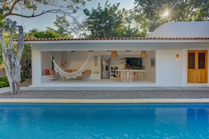 A modern house with a pool, a hammock, and a dining area.