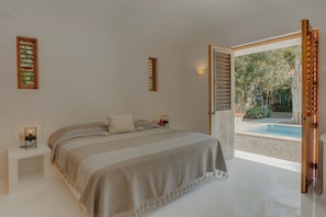 A bedroom with a bed, bedside tables, a nightstand, a window with a view of a pool, and a door leading outside.