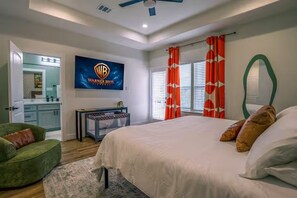 Une chambre à coucher avec un lit, un fauteuil vert, une coiffeuse avec un miroir et une affiche de film Warner Bros accrochée au mur.