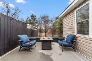 An outdoor patio with two wicker chairs, a fire feature, and a view of the backyard.