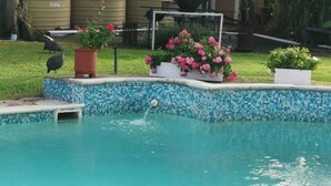 A swimming pool with a mosaic tile edge, surrounded by potted plants and a grassy yard. - Room-joy's Place - Willy's Cottage - 2 S (Cape Town)
