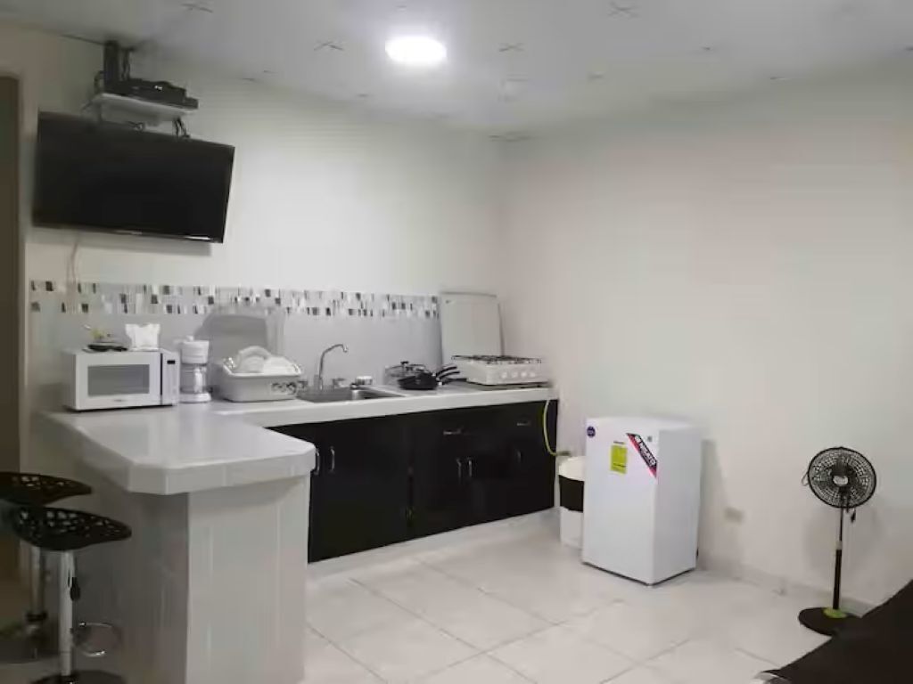 A kitchen with a microwave, stove, refrigerator, and a fan.. Shop-Changuinola-Fit5people