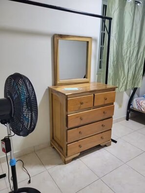 A wooden dresser with drawers, a mirror, and a standing fan in a room with a tiled floor. - Shop-Changuinola-Fit5people (Changuinola)