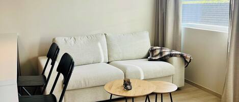 A living room with a sofa, two chairs, a coffee table, and a window with curtains.