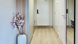 En hall med trägolv, en vit vas med rosa blommor, en stor spegel och en dörr längst ner.