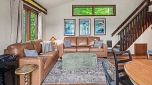 Un salon avec deux canapés en cuir marron, un pouf vert, un tapis à motifs et une table à manger en bois avec des chaises.