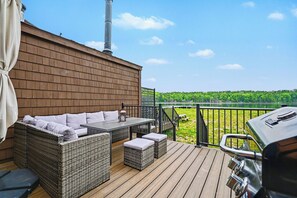 Una terraza con mobiliario de mimbre, una parrilla y vistas a un paisaje verde.