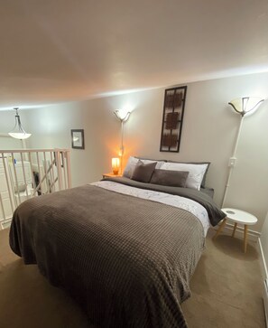 A bedroom with a large bed, two bedside lamps, a wall-mounted artwork, and a small table.