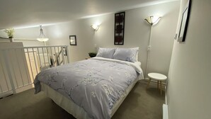 A bedroom with a bed, bedside lamps, a small table, and a radiator.