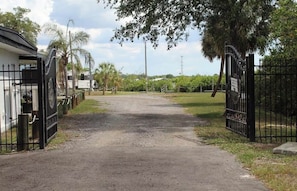 A gated entrance to a property with a gravel driveway, palm trees, and a clear sky. - Harbor Haven #5 (Riverview)