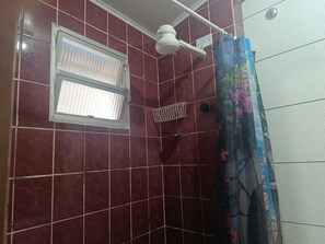 Une douche avec une pomme de douche blanche fixée au plafond, une fenêtre avec des stores et un rideau de douche à motifs floraux.