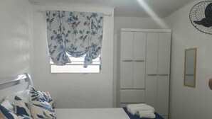 Quarto com cama, guarda-roupa, janela com cortinas e ventoinha.