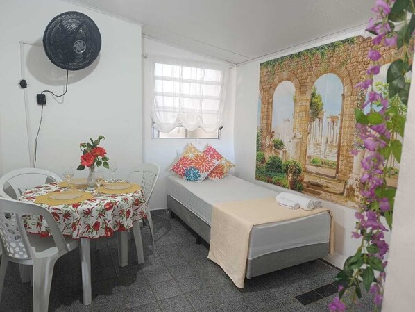 Une pièce avec un lit, une table et des chaises, un ventilateur et une fenêtre.