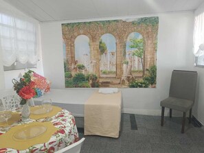 Une pièce comprenant une table à manger dressée pour quatre personnes, un banc, une chaise et une grande fresque représentant un arc antique.