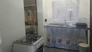 Uma cozinha compacta com fogão a gás, pia e janela com cortinas de renda.