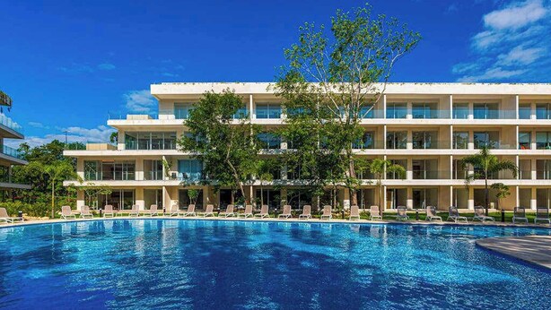 Hotel com piscina, vários andares e céu azul límpido.