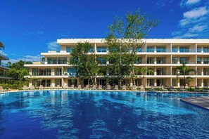 Een hotel met een zwembad, meerdere verdiepingen en een helderblauwe lucht.