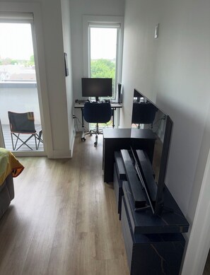 Et værelse med et klaver, et skrivebord med en computer, en stol og et vindue med udsigt.