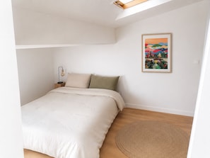 Ein Schlafzimmer mit einem Bett, einem Nachttisch, einer Lampe, einem runden Teppich und einem gerahmten Bild an der Wand.