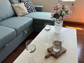 A living room with a grey sofa, a white coffee table, two wine glasses, a vase with flowers, and a water pitcher. - * Coastal Paradise: Your relaxing corner by the beach (O Pindo)