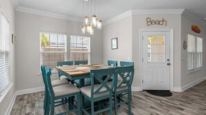 Ein Esszimmer mit Holztisch und stuhlfarbenen Sesseln, einer Chandelüstere und einer Tür mit der Aufschrift 'Beach'.