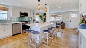 Uma cozinha moderna com armários brancos, uma ilha central com banquetas e iluminação pendente.