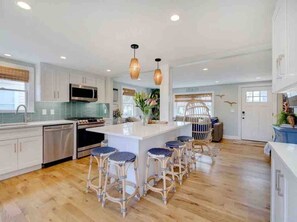 Una cocina moderna con armarios blancos, una isla central con taburetes y lámparas colgantes.
