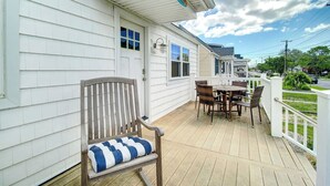 Um deck de madeira com uma cadeira de balanço e uma mesa com cadeiras, um cercado branco e uma casa com revestimento branco.