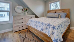 Quarto com cama, cômoda, ventoinha de teto e janelas.