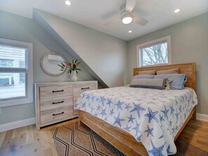Un dormitorio con cama, cómoda, ventilador de techo y ventanas.