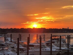 Ein Yachthafen mit vertäuten Booten, im Hintergrund ein Sonnenuntergang und eine ruhige Wasseroberfläche.