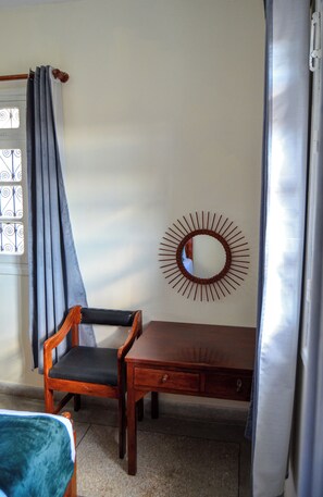 Une pièce comprenant une chaise en bois, une table, un miroir et une fenêtre avec des rideaux.