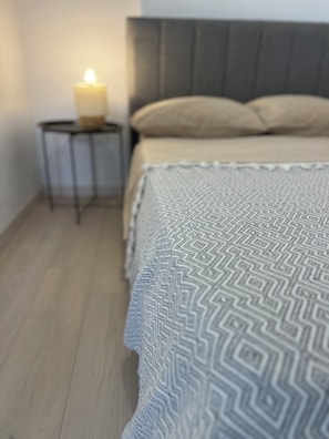 Un lit recouvert d’une couverture à motifs, une table de chevet avec une bougie et un plancher en bois.