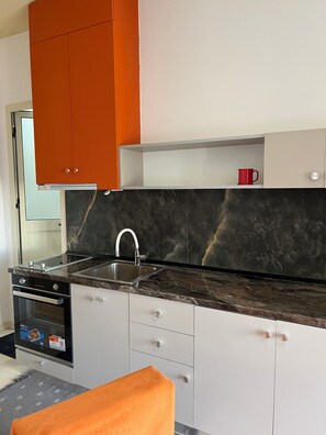 Una cocina moderna con encimera de mármol negro, pileta de acero inoxidable y muebles blancos.