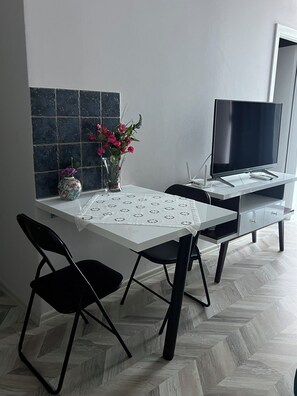 A dining area with a table, chairs, a vase with flowers, a flat-screen TV, and a herringbone-patterned floor. - Fabulous 11-bedroom hotel in Heart of Shkodër.AC ,High-speed Wi-Fi.Comfort,style (Shkodër)